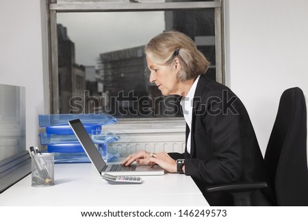 Side view of senior businesswoman using laptop at desk in office