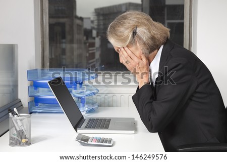 Side view of tired senior businesswoman in front of laptop at desk in office