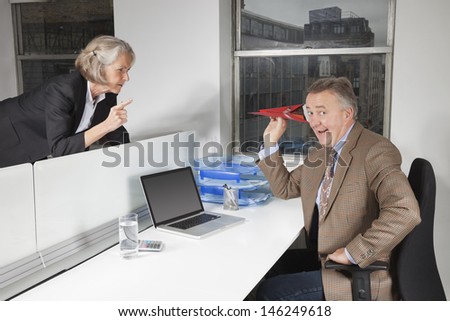 Middle-aged businessman throwing paper airplane towards female colleague in office