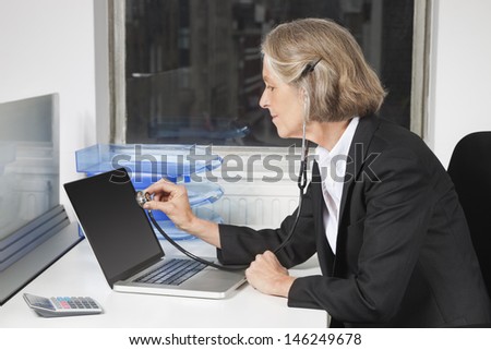 Side view of senior businesswoman examining laptop with the use of stethoscope at office desk