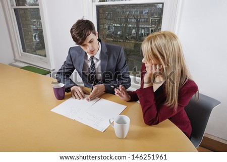 Young businessman and female colleague with paperwork at conference table