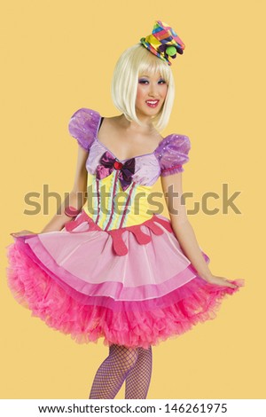 Portrait of young woman in doll\'s costume posing against yellow background