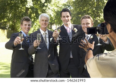 Man taking a picture of five men toasting with wine glasses at wedding party