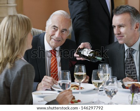 Three businesspeople talking at restaurant table as waiter serves wine