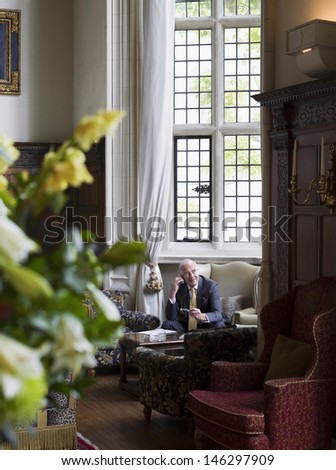 Mature businessman sitting on antique furniture and using cellphone