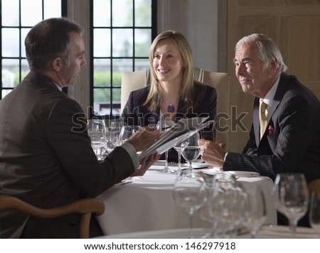 Three businesspeople sitting at restaurant table and discussing documents