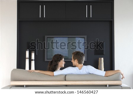 Romantic young couple looking at each other while relaxing on couch in living room