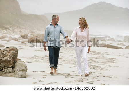 Full length of happy couple holding hands while walking on beach