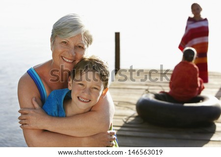 Portrait of happy senior woman hugging grandson on jetty with sisters in background