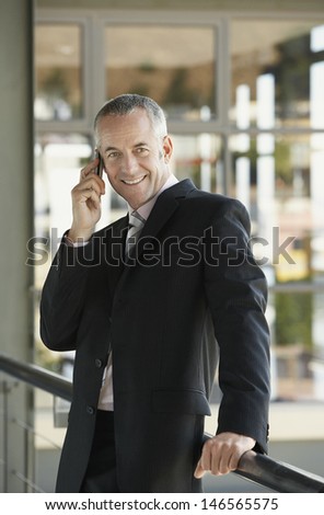 Portrait of happy middle aged businessman using cell phone in office