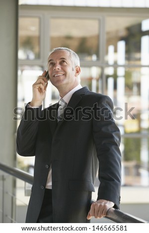 Happy middle aged businessman using cell phone while looking up in office