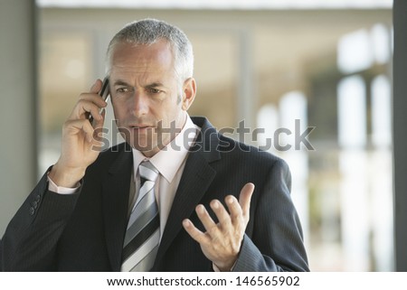 Serious middle aged businessman gesturing while using cell phone in office