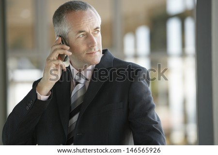 Confident middle aged businessman using cell phone in office