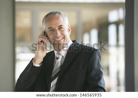 Happy middle aged businessman using mobile phone in office