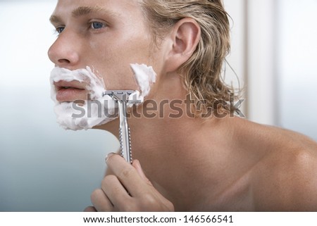 Closeup of handsome young man shaving in bathroom