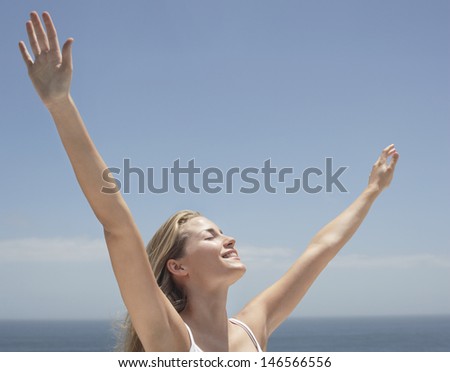Happy young woman with arms outstretched and eyes closed against ocean