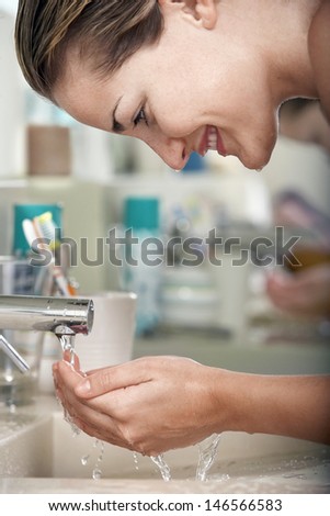 Closeup of happy young woman washing face in bathroom