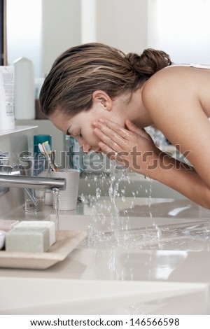 Closeup of beautiful young woman washing face in bathroom