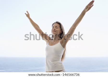Young woman with arms outstretched and eyes closed standing against ocean