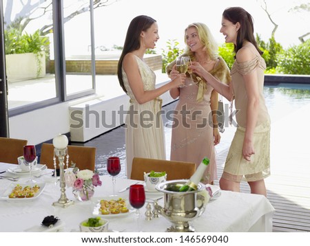 Three young female friends toasting champagne flutes at dinner party