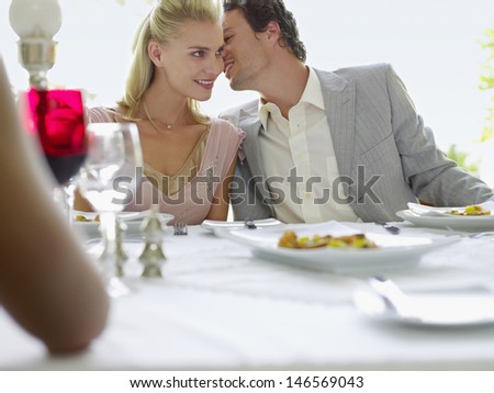 Young man whispering into woman\'s ear at dinner party