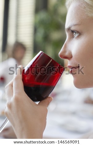 Closeup of happy young woman drinking red wine at dinner party