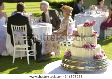 Closeup of weeding cake with guests at tables in background