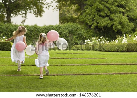 Rear view of little bridesmaids with balloons running in garden
