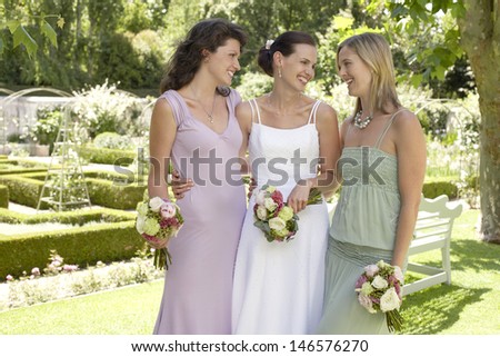 Cheerful bride with female friends holding bouquets in formal garden