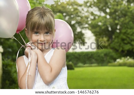 Portrait of cute little bridesmaid holding balloons in garden