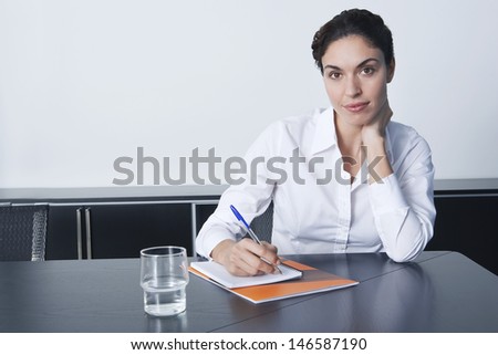 Portrait of beautiful young businesswoman writing notes at conference table