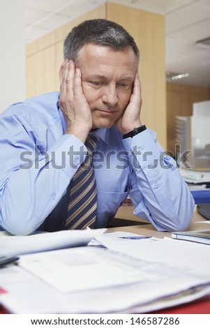 Pensive middle aged businessman sitting at office desk