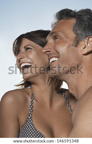 Closeup side view of a cheerful couple laughing against sky
