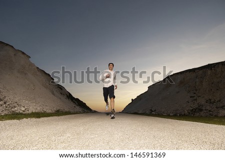 Full length of a young man jogging on country street at dusk