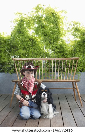 Full length portrait of a smiling boy in cowboy costume kneeling with dog on deck