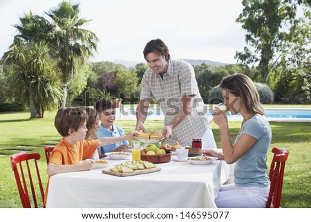 Couple with three children sitting at breakfast table outdoors