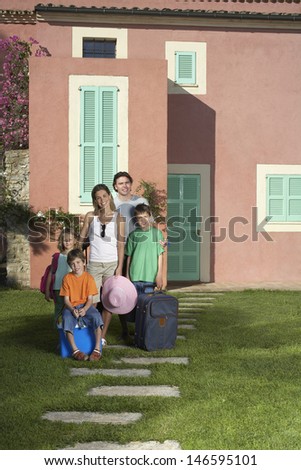 Full length portrait of a couple with three children and luggage in front of house