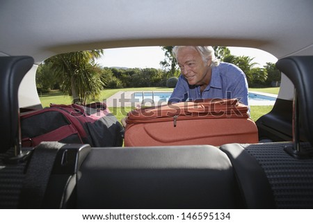View of senior man putting luggage into car boot