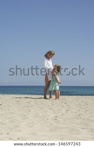 Full length side view of a mother and daughter standing face to face on sunny beach