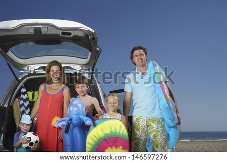Portrait of a smiling couple with three children at beach by car