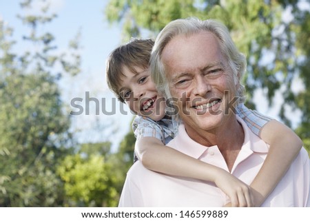 Closeup portrait of a smiling grandfather with grandson riding piggyback outdoors