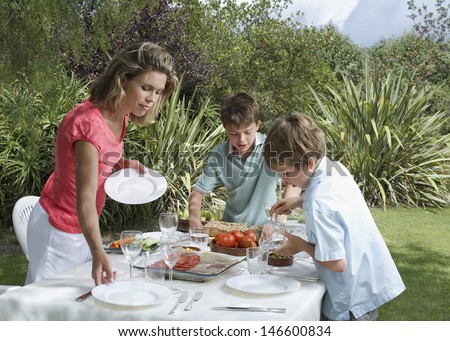 Mother and two sons setting the dinner table in garden