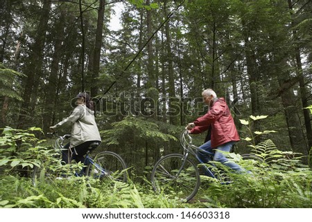 Low angle side view of mature man and middle aged woman with bikes on forest road