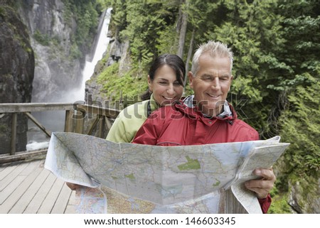 Mature man and woman reading map with waterfall in the background