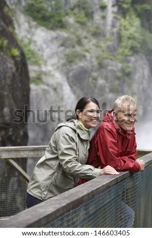 Side view of a smiling middle aged man and woman leaning on outdoor railing