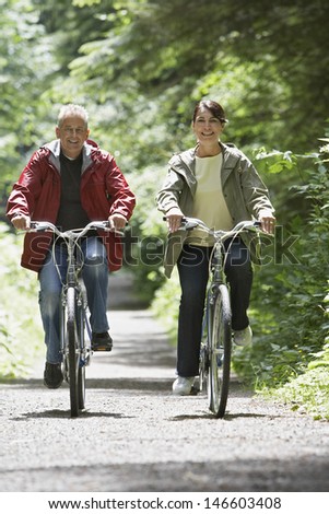 Full length of a mature man and middle aged woman biking on forest road