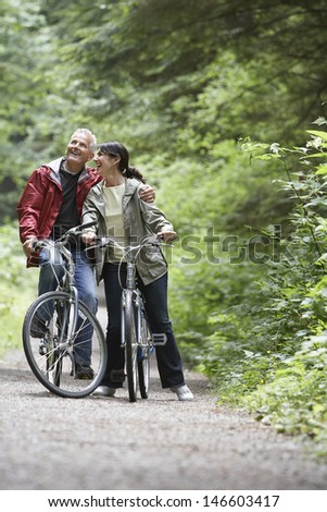 Cheerful mature man and middle aged woman with bikes on forest road
