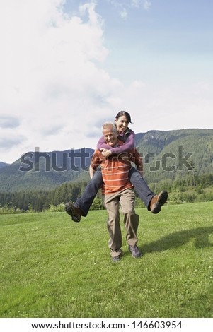 Full length of an active middle aged man carrying woman on back on meadow