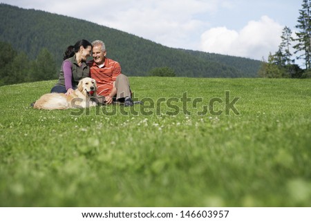 Happy middle aged couple and golden retriever relaxing on grass