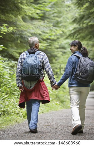 Full length rear view of a couple walking on forest road amid lush trees